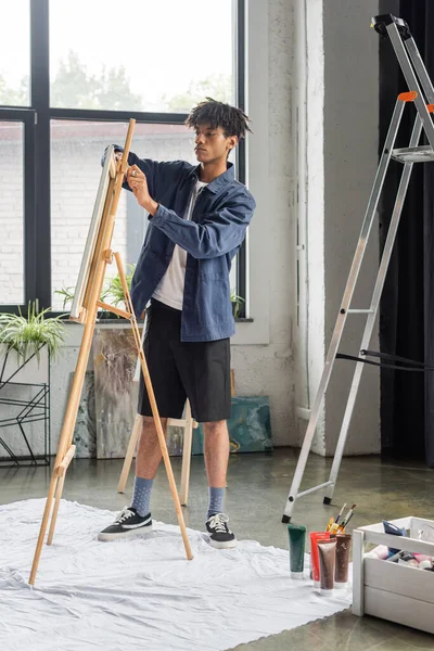 African american artist fixing canvas on easel in workshop — Stock Photo