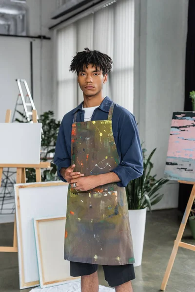 Young african american artist in apron looking at camera in workshop — Stock Photo