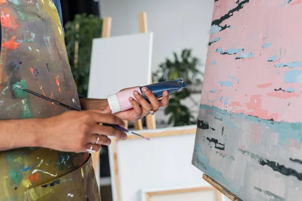 Ausgeschnittene Ansicht eines afrikanisch-amerikanischen Künstlers in Schürze mit Farbtusche und Pinsel in der Nähe der Zeichnung — Stockfoto