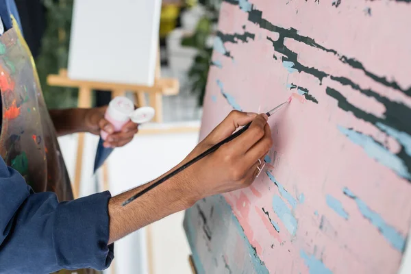 Ausgeschnittene Ansicht eines afrikanisch-amerikanischen Künstlers in Schürzenmalerei auf Leinwand im Atelier — Stockfoto