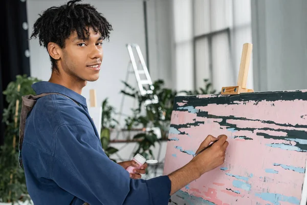 Smiling african american artist painting on canvas in studio — Stockfoto