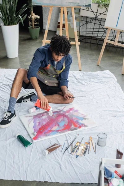 Afroamerikanischer Künstler gießt im Atelier Farbe auf Leinwand auf Tuch — Stockfoto