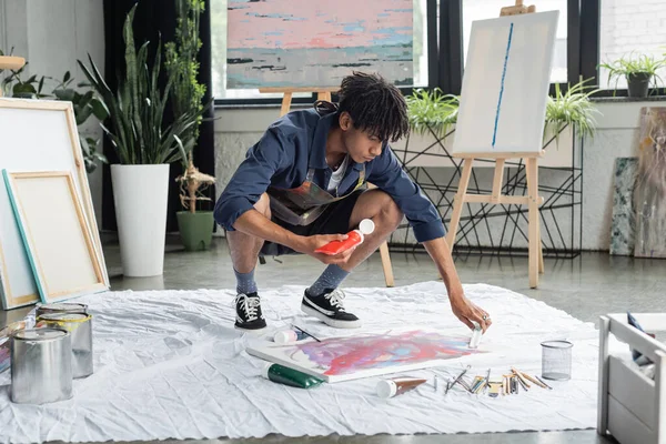 Африканский художник держит краску возле холста и кисти на ткани в студии — стоковое фото