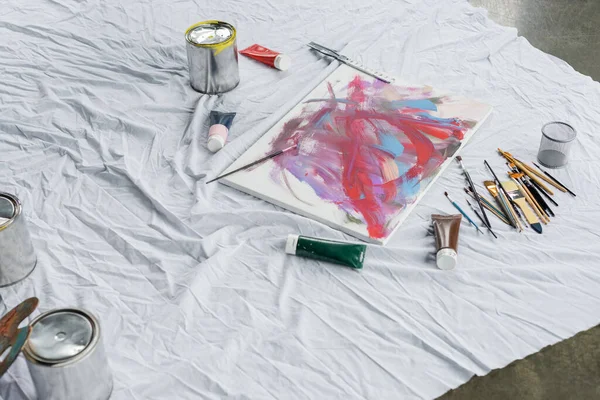 High angle view of canvas near paints and paintbrushes on cloth in workshop — Stock Photo