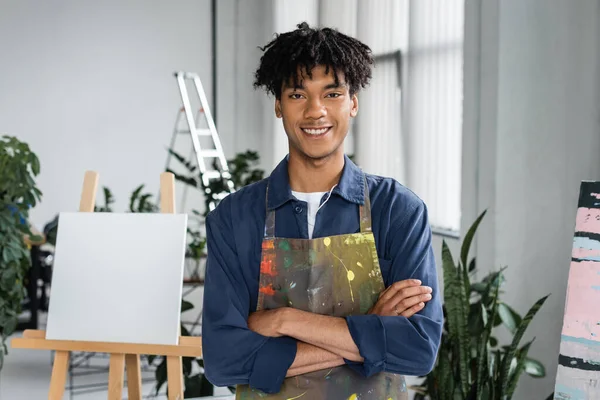 Smiling african american artist crossing arms and looking at camera in workshop — Stock Photo