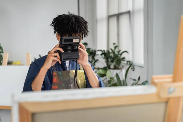 African american artist taking photo on vintage camera near blurred canvas in studio — Stock Photo