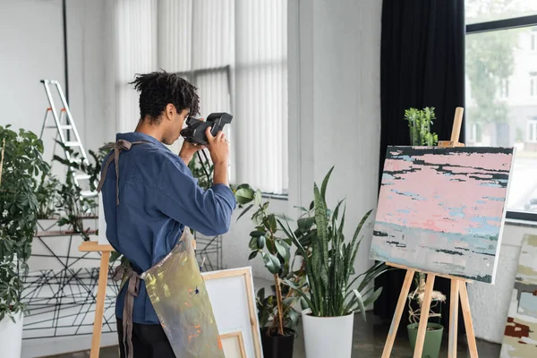 African american artist taking photo on vintage camera near painting in studio — Stock Photo
