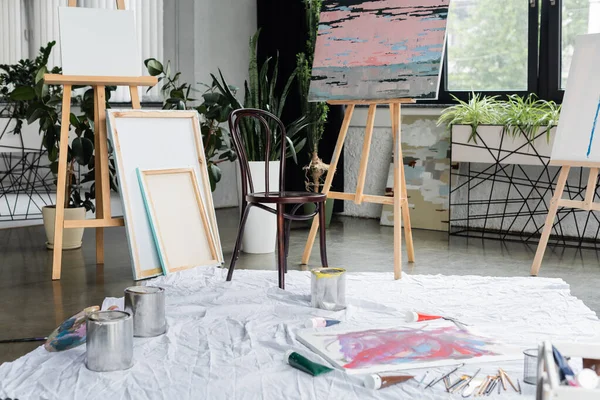 Canvases near paints and paintbrushes on floor in studio - foto de stock