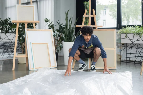 Jovem artista afro-americano colocando celofane no chão em estúdio — Fotografia de Stock