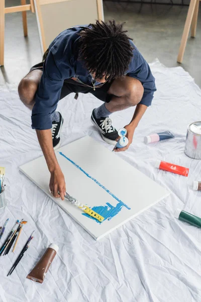 African american artist in apron painting with spatula on canvas in studio — Stockfoto