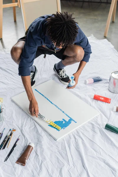 African american artist in apron painting with spatula on canvas in studio — Foto stock