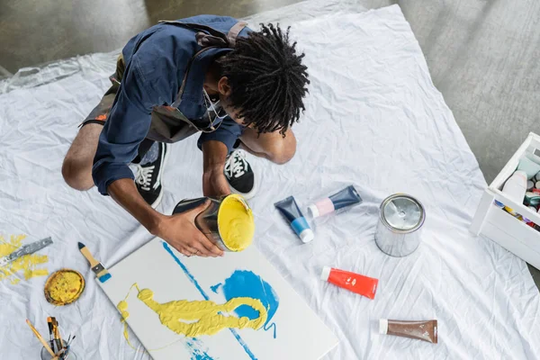 Overhead view of african american artist pouring paint on canvas in studio — Stock Photo