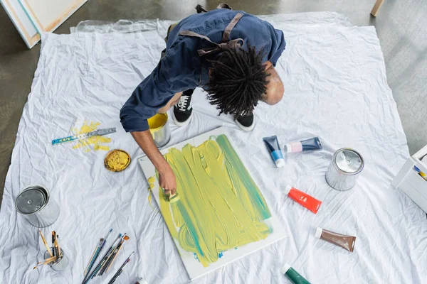 Overhead view of african american artist painting on canvas on floor — Stock Photo