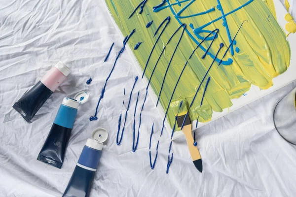 Top view of acrylic paints near canvas and paintbrush on cloth — Stock Photo