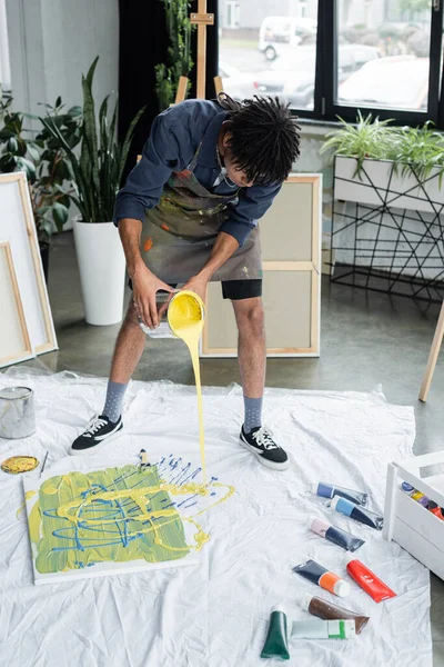 Artiste afro-américain versant de la peinture sur tissu près de la toile en studio — Photo de stock