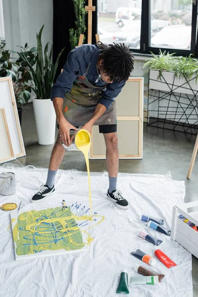 African american artist pouring paint on cloth near canvas in studio — Stock Photo