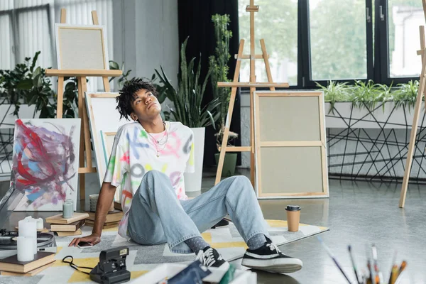 Проникливий афроамериканець сидить біля смартфона і книг у художній студії. — стокове фото