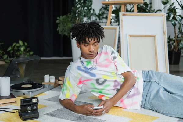 African american artist using smartphone near vintage camera and blurred canvases — Stock Photo