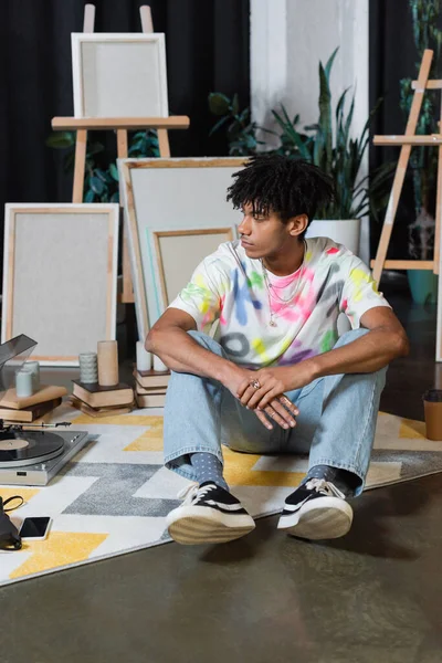 African american artist sitting near smartphone and record player in studio — стокове фото
