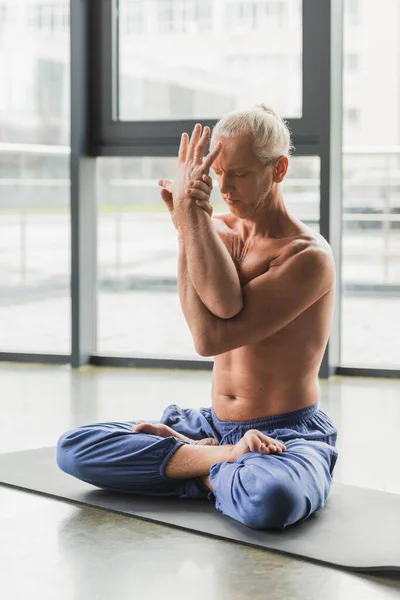 Barefoot man in blue pants sitting with closed eyes in lotus pose - foto de stock