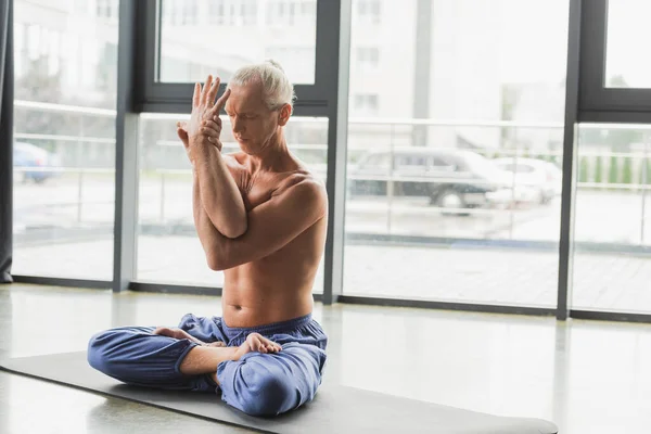Focused man in blue pants sitting with closed eyes in lotus pose — Stock Photo