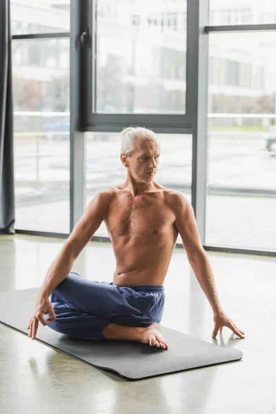 Grey haired man in pants sitting in half lord of fishes pose in studio — Stock Photo