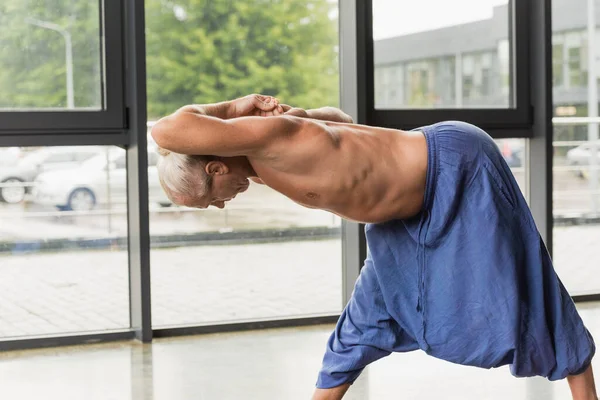 Flexible and grey haired man doing standing forward bend pose in yoga studio — Stock Photo