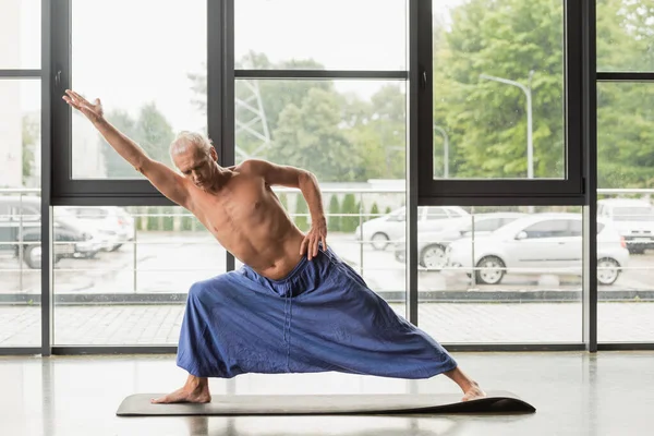 Shirtless and grey haired man doing extended side angle pose in yoga studio — Stock Photo