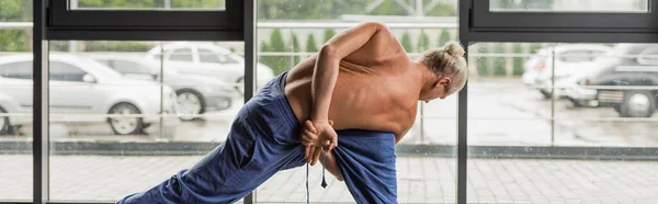 Grey haired man in pants doing twist lunge yoga pose in studio, banner — Stock Photo