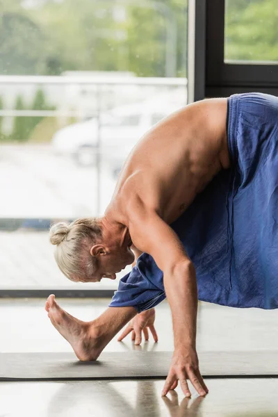 Vista laterale di uomo dai capelli grigi facendo posa piramide sul tappeto in studio di yoga — Foto stock