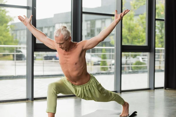 Hombre sin camisa y descalzo en pantalones verdes practicando salto yoga pose en estudio - foto de stock