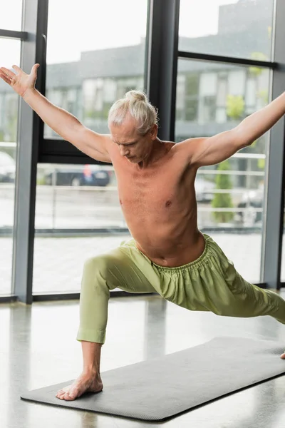 Uomo senza maglietta in pantaloni verdi praticando lunge yoga posa in studio — Foto stock