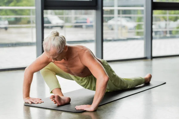 Homme aux cheveux souples et gris faisant assis courbure vers l'avant sur tapis de yoga en studio — Photo de stock