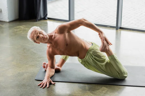 Uomo senza maglietta che fa supina torsione spinale posa yoga in studio — Foto stock