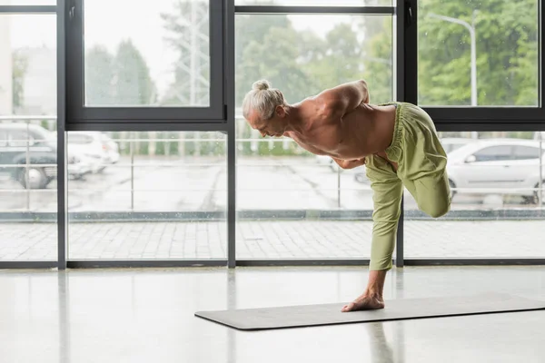 Hemdloser und barfüßiger Mann posiert im Yoga-Studio mit halb gebundenen Lotusbäumen — Stockfoto