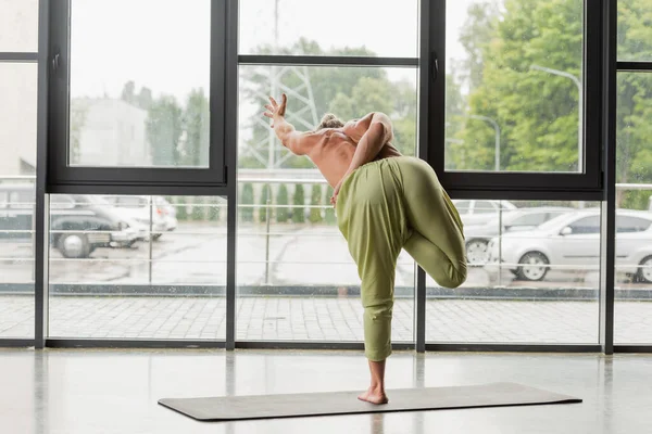 Visão traseira do homem sem camisa fazendo metade da pose de árvore de lótus encadernada no estúdio de ioga — Fotografia de Stock