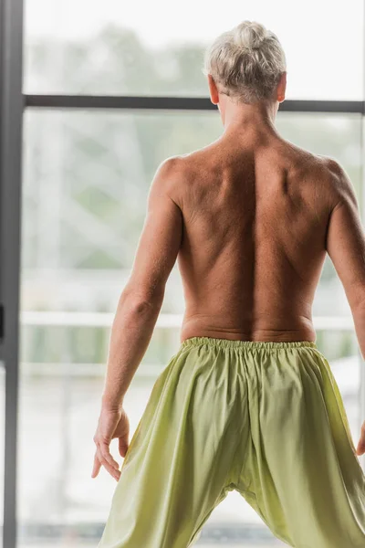 Back view of shirtless man in green pants standing in yoga studio — Stock Photo