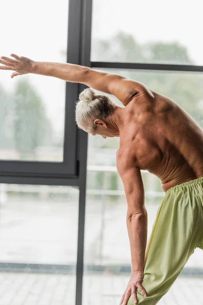 Back view of shirtless man in green pants doing side bend in yoga studio — Stock Photo