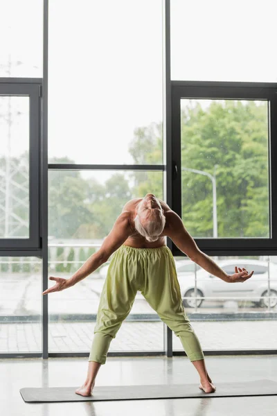 Полная длина мужчина без рубашки в зеленых брюках делает заднюю изгиб в студии йоги — стоковое фото