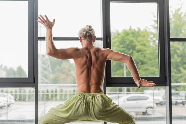 Мужчина без рубашки в зеленых штанах позирует богине во время жеста в студии йоги — стоковое фото