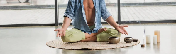 Abgeschnittene Ansicht eines Mannes in Lotus-Pose beim Meditieren in der Nähe tibetischer Klangschalen im Yoga-Studio, Banner — Stockfoto
