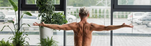 Rückenansicht eines hemdslosen Mannes, der mit ausgestreckten Händen im Yogastudio sitzt, Banner — Stockfoto