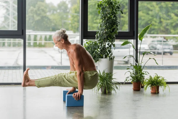 Homem sem camisa em calças verdes fazendo pose vaga-lume em blocos de espuma de ioga — Fotografia de Stock
