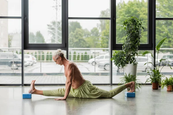 Vista lateral do homem sem camisa e cabelos grisalhos fazendo divisão em blocos de espuma de ioga — Fotografia de Stock