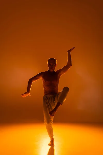 Full length of shirtless man in pants practicing yoga on orange background — Stock Photo