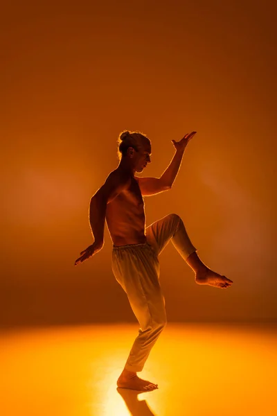 Side view of shirtless man in pants practicing yoga on orange background — Stock Photo