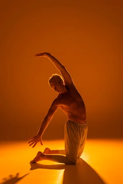 Повна довжина без сорочки, що стоїть на колінах, практикуючи йогу на коричневому фоні — стокове фото