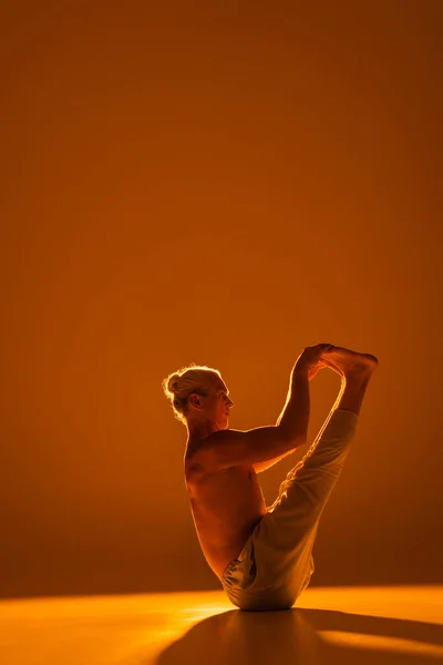 Longitud completa de hombre sin camisa haciendo barco yoga pose en marrón - foto de stock
