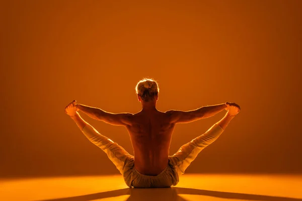 Back view of shirtless man doing sitting hands to toes yoga pose on brown — Fotografia de Stock