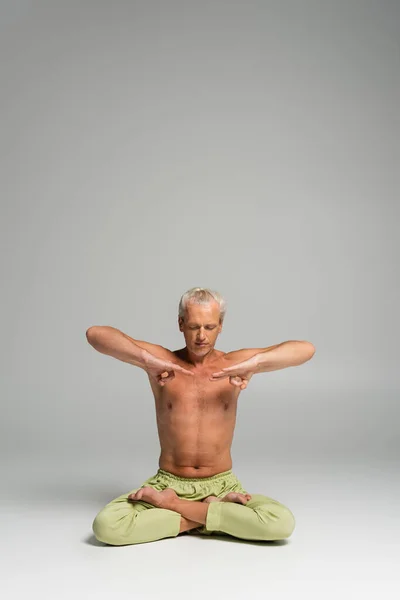 Homme torse nu avec les yeux fermés assis dans la pose de lotus sur fond gris — Photo de stock